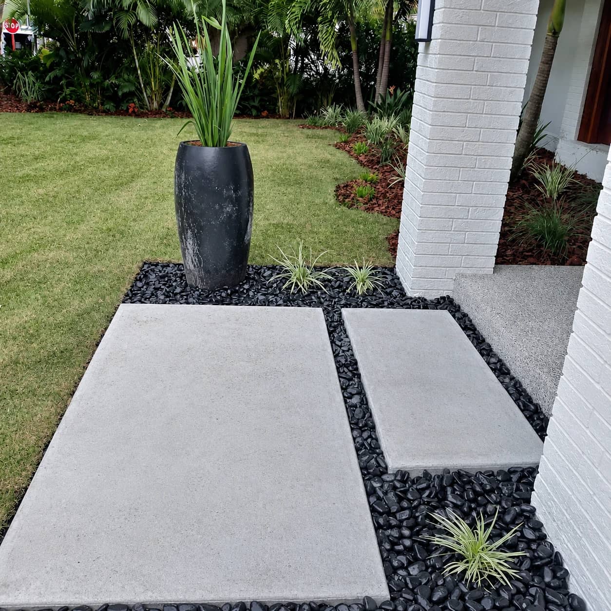 Modern hardscape entry with concrete pavers, black landscape rock, and plant accents.