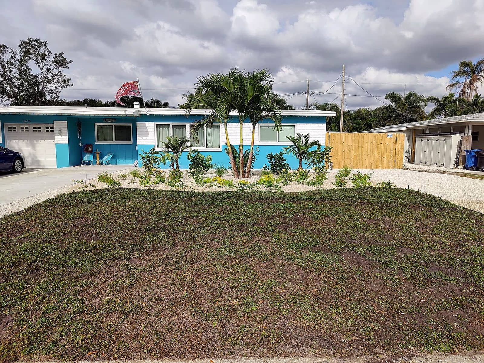 Refreshed front yard with new palm trees, fresh plantings, and clean garden beds in front of a home.